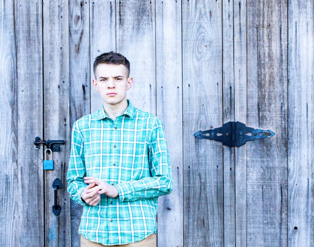 Senior Photography of a Male student shot with a 24mm - 70mm lens against a wooden barn